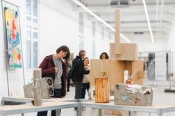 A woman smiles as she looks at the abstract sculptures in a bright, modern art gallery. Several people can be seen in the background and colourful works of art hang on the walls.