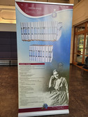 A vertical display panel about Edith Stein shows a large photo of her seated, a collection of book spines in the upper section, a text with a description of her works and a decorative floral graphic in the lower section.
